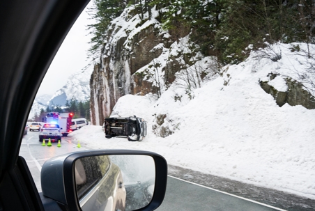 Car driving by a vehicle accident being attended to by emergency crews on the side of a slippery highway in winter